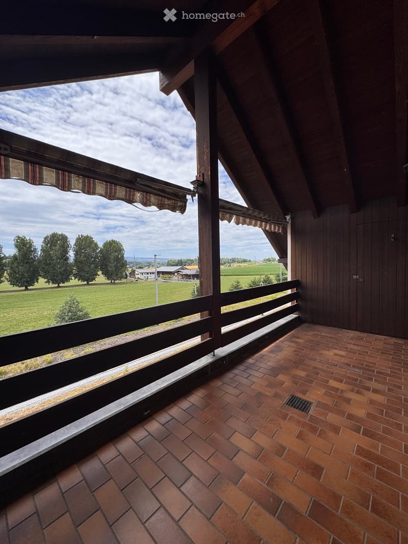 Balcony with brick tiles, wooden railing, and scenic countryside view.