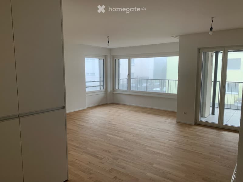 Empty room with wooden flooring, large windows, and sliding glass doors leading to a balcony.