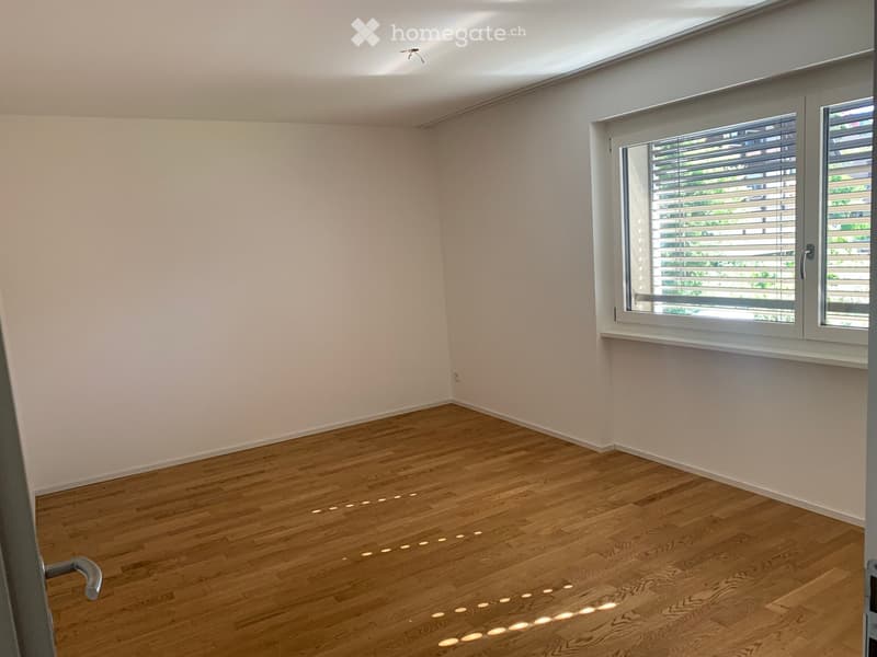 Empty room with light wooden flooring and white walls, featuring large windows with blinds and recessed ceiling lighting.