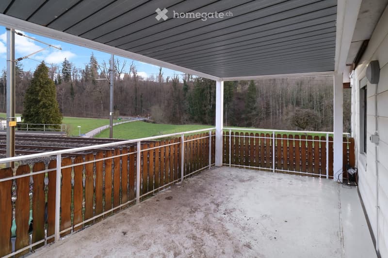 Balcony with wooden fence, metal railing, and a view of a green field and trees.