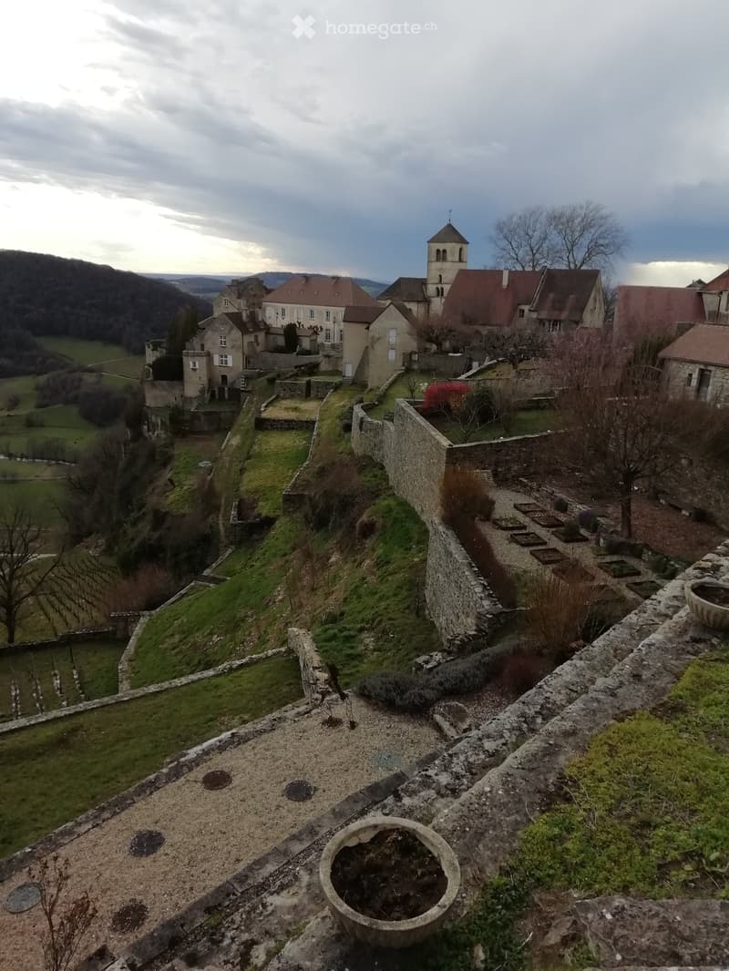 View from a castle rooftop showing stone walls, a church tower, and surrounding countryside with fields and trees.