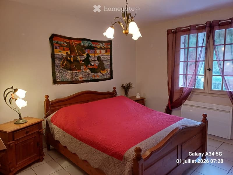 Cozy bedroom with a wooden bed, red quilt, nightstands with lamps, and a decorative wall tapestry.