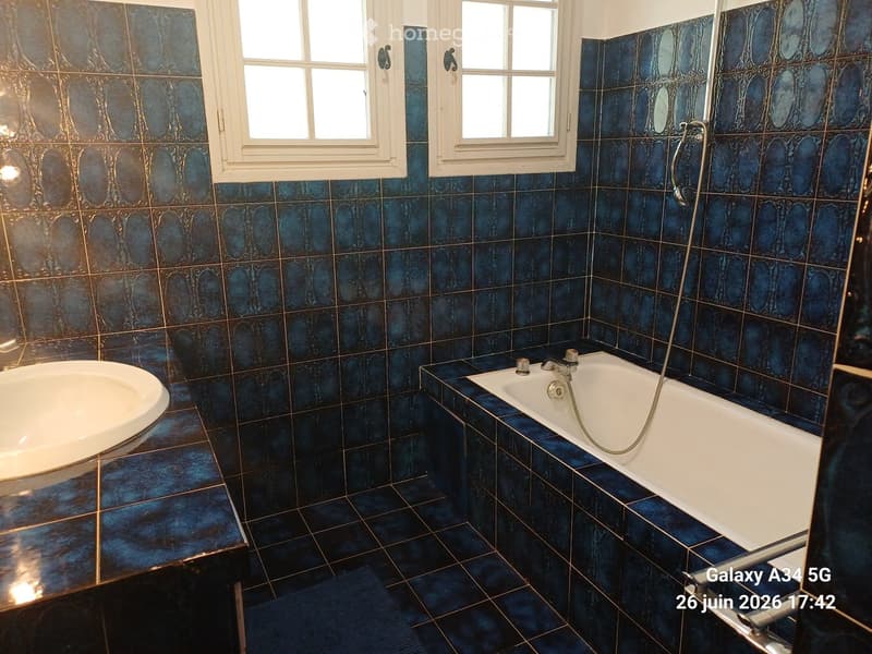 Bathroom with blue patterned tiles, a white bathtub, and a white sink.
