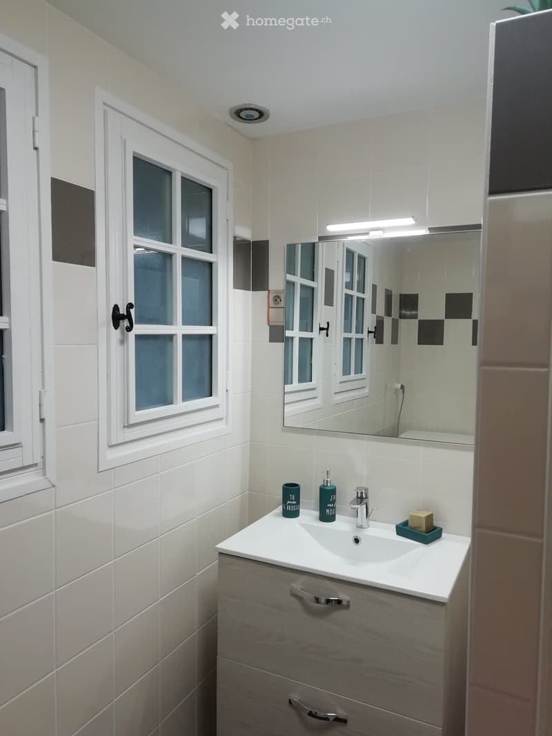 Modern bathroom with white tiles, a large mirror, a sink with a modern faucet, and a small window with frosted glass panes.