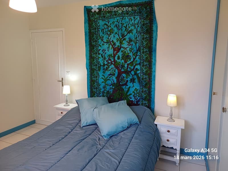 Bedroom with a neatly made bed, two nightstands with lamps, and a colorful tapestry on the wall.