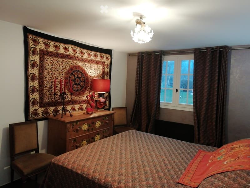 Cozy bedroom with a patterned bedspread, wooden nightstand, table lamp, decorative tapestry, and a chandelier.