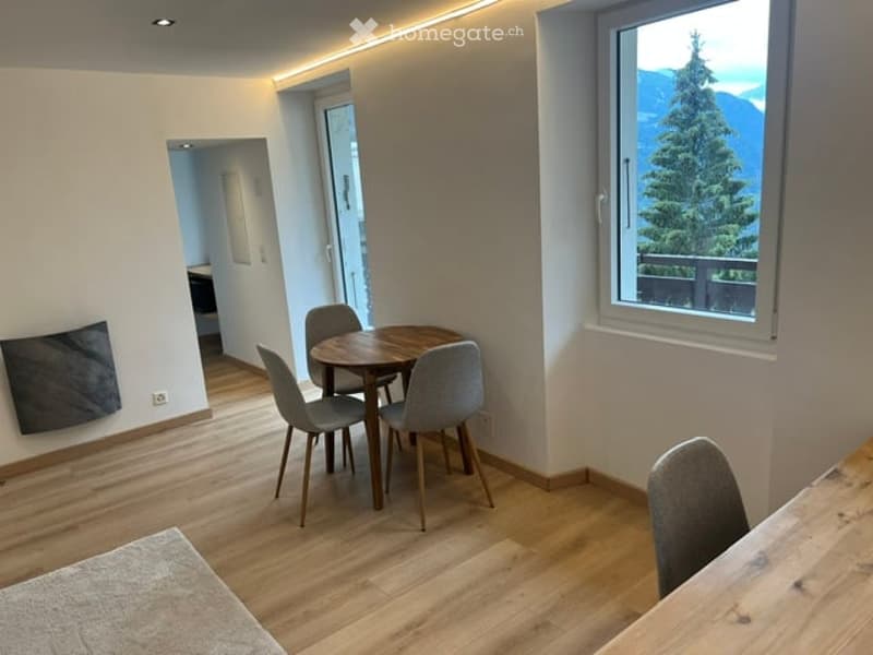 Bright dining area with wooden floor, round dining table, four chairs, large window with mountain view, and modern lighting.