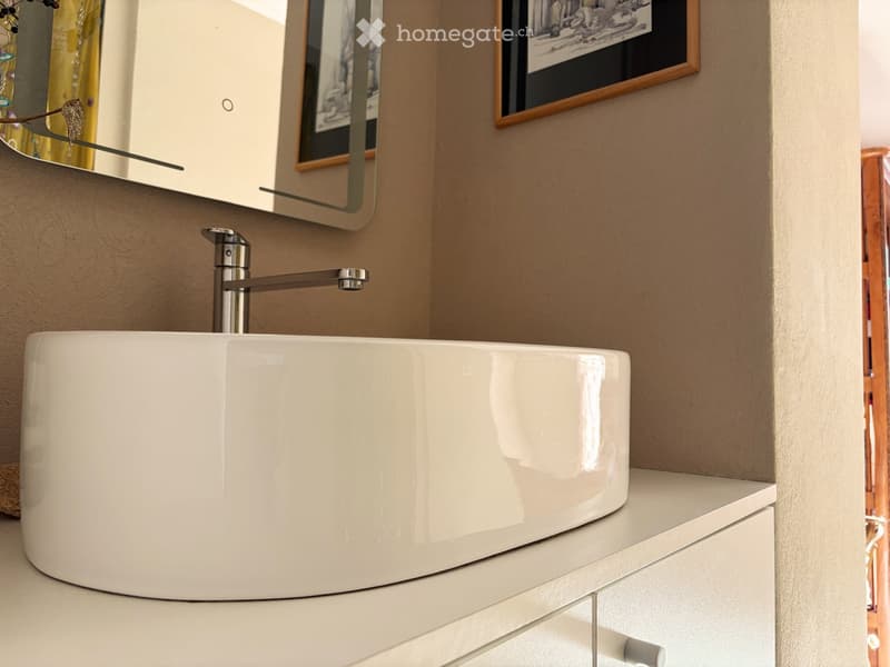 Modern bathroom, white basin, silver faucet, mirror, picture frame, white cabinetry, wooden door, tiled wall