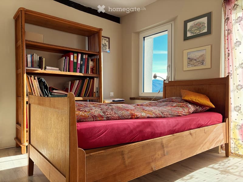 wooden bed, two pillows, two mattresses, wooden bookshelf, books, picture frames, lamp, window, natural light, hardwood floor