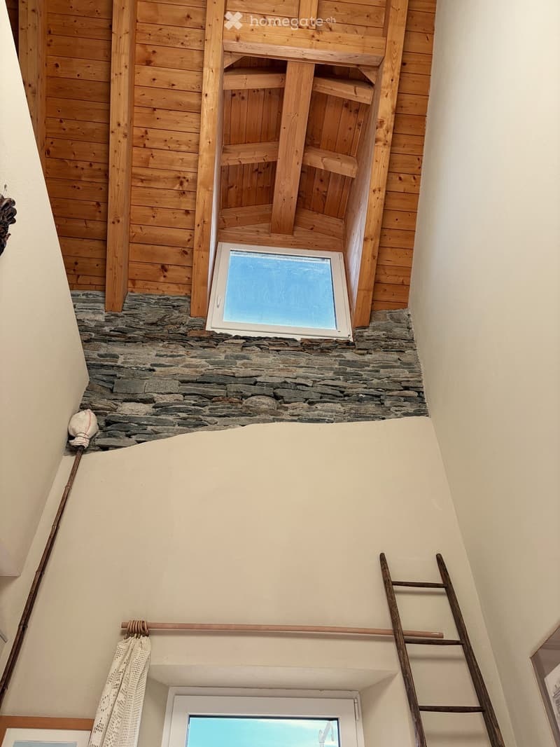 Wooden ceiling beams, stone wall, attic window, wall-mounted ladder, curtain rod, floor-mounted curtain