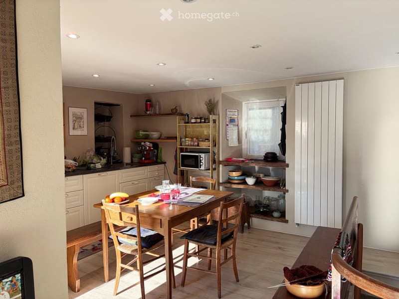 A dining area with a wooden table and chairs, surrounded by shelves and a microwave.