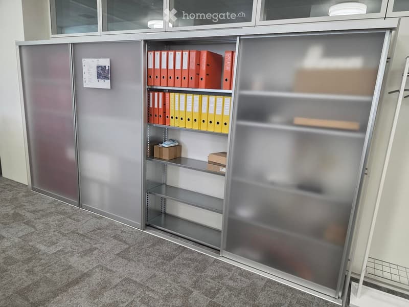 Metal cabinet with glass doors and shelves filled with red and yellow folders, small boxes, and a notepad on the floor.