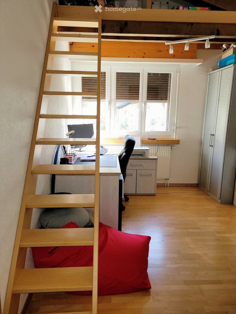 A multi-functional room with a wooden staircase leading to a loft area, a desk with a laptop and printer, a chair, a padded seat, and a cabinet.
