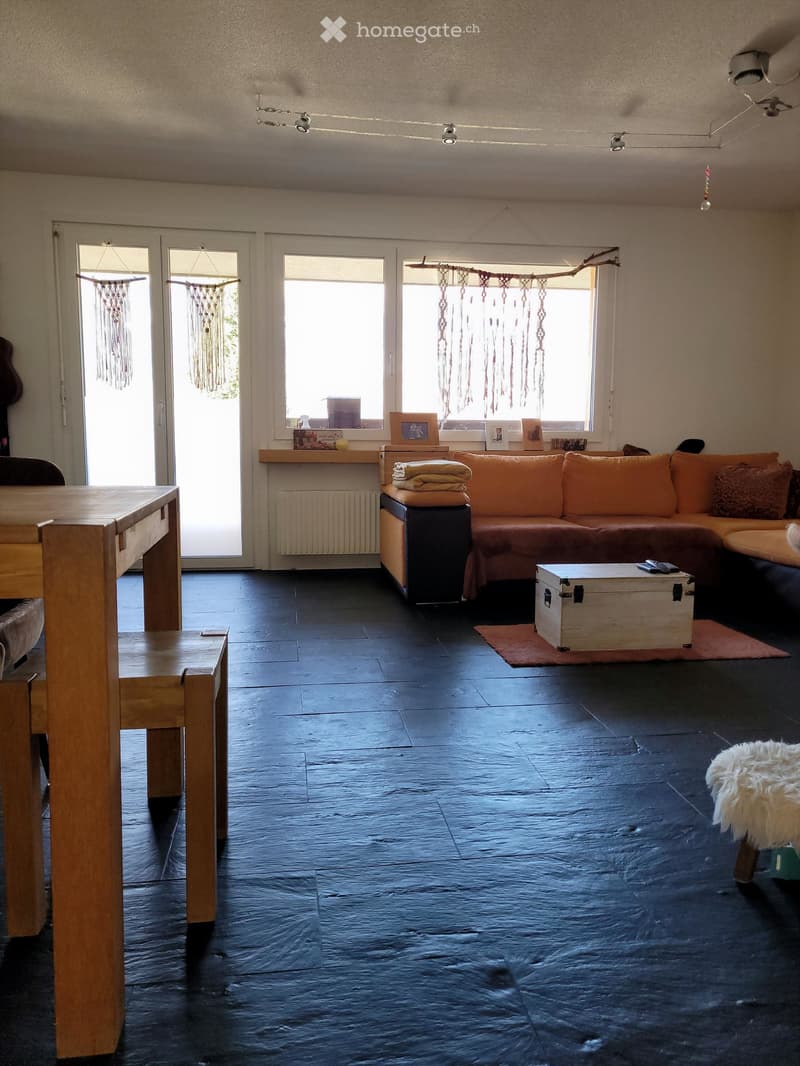 Living room with dark tiled floor, large windows, orange sofa, coffee table, wooden table, and decorative items on the windowsill.