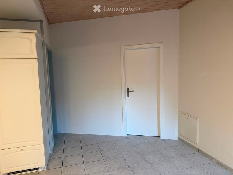 Empty room with tiled floor, white walls, and a closed door. A built-in cabinet is visible on the left side.