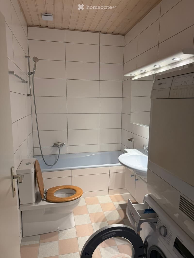 Bathroom with white tiles, wooden ceiling, toilet, bathtub, sink, washing machine