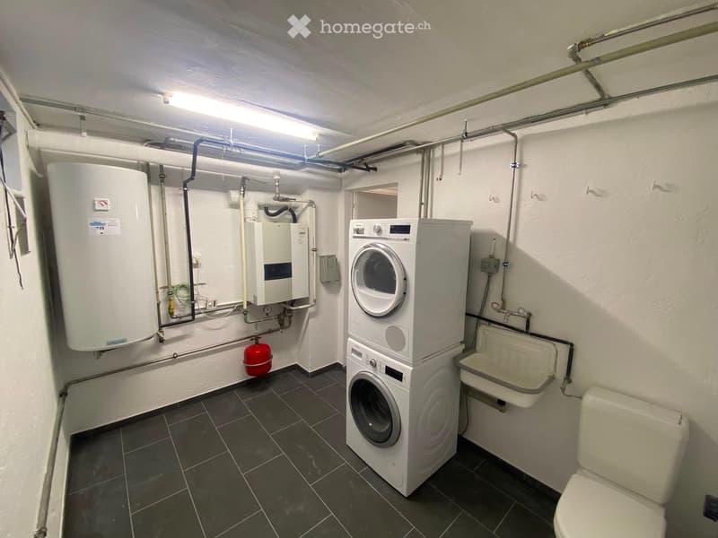 Utility bathroom with a washing machine, toilet, water heater, and sink, featuring exposed pipes and a tiled floor.