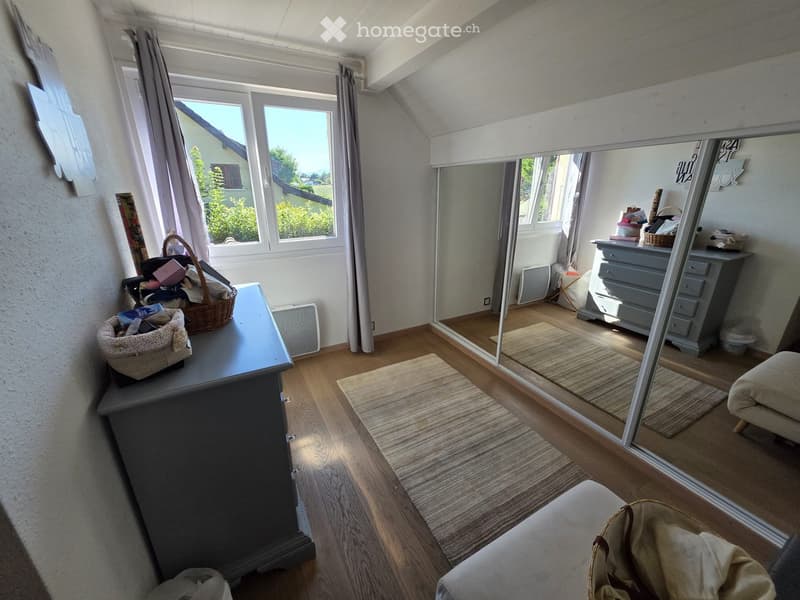 A well-lit room with wooden flooring, large windows, a sofa, a table with baskets, a mirror, and a dresser with drawers.