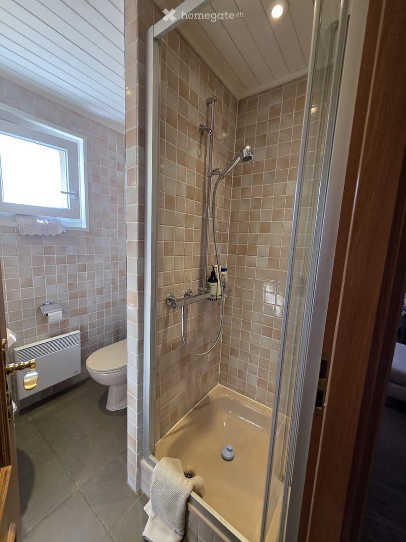 Bathroom with a toilet, bathtub, shower, towel, radiator, and a window with blinds.