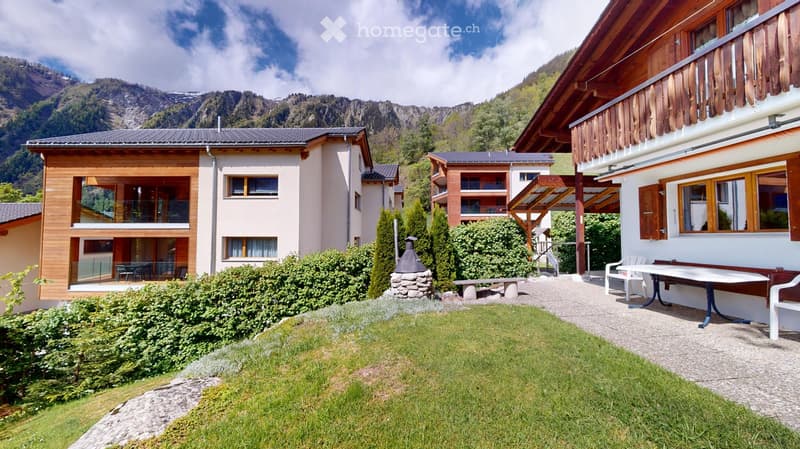 A well-maintained garden area with a lawn, patio furniture, and a scenic mountain view in the background.