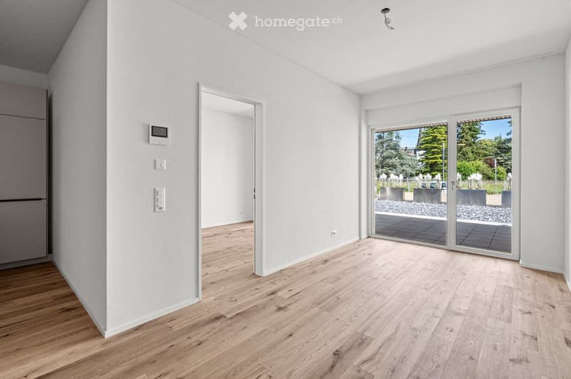 Empty room with light wooden flooring, white walls, and large sliding glass doors leading to an outdoor area.