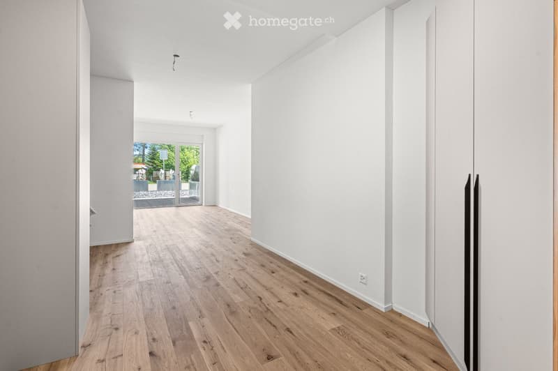 Empty hallway with light wooden flooring and white walls, featuring a large glass door leading to an outdoor area.