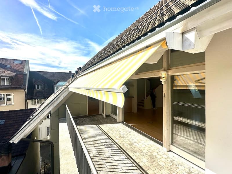 A covered balcony on a building with a brick wall, yellow and white awning, and glass door.