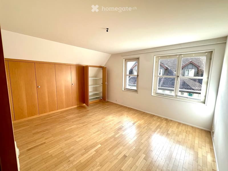 Empty room with wooden floor, white walls, wooden cabinets, and two windows