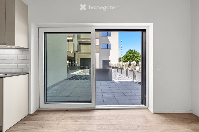 Empty room with wooden flooring, white walls, and a large sliding glass door leading to a tiled outdoor area.