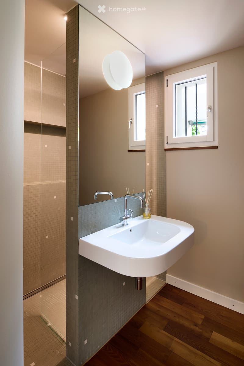 Modern bathroom with a white sink, chrome faucet, large mirror, and wooden flooring.