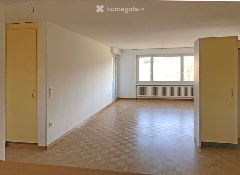Empty room with wooden flooring, white walls, large windows, and a radiator. No furniture or equipment present.
