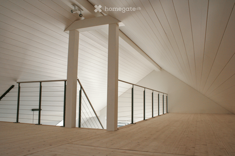Open, minimalist space with wooden flooring, white paneled walls, and a modern metal railing leading to another level. No furniture or equipment visible.