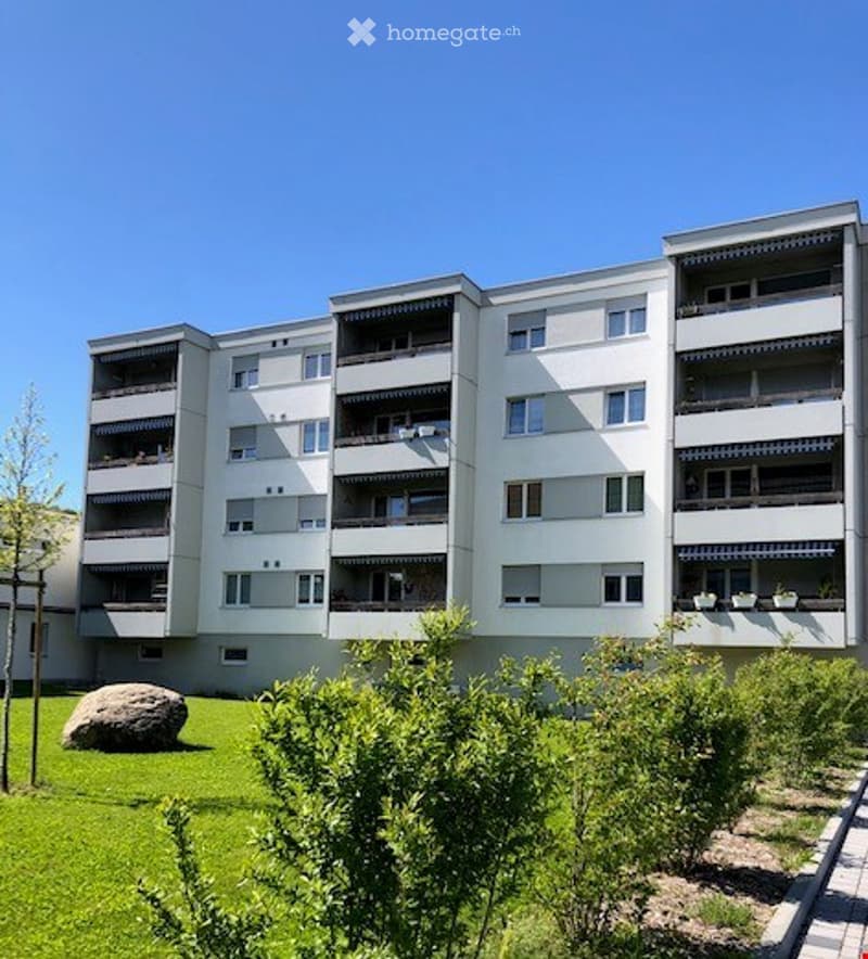 5 story apartment building, white, multiple balconies, garden in front, large rock