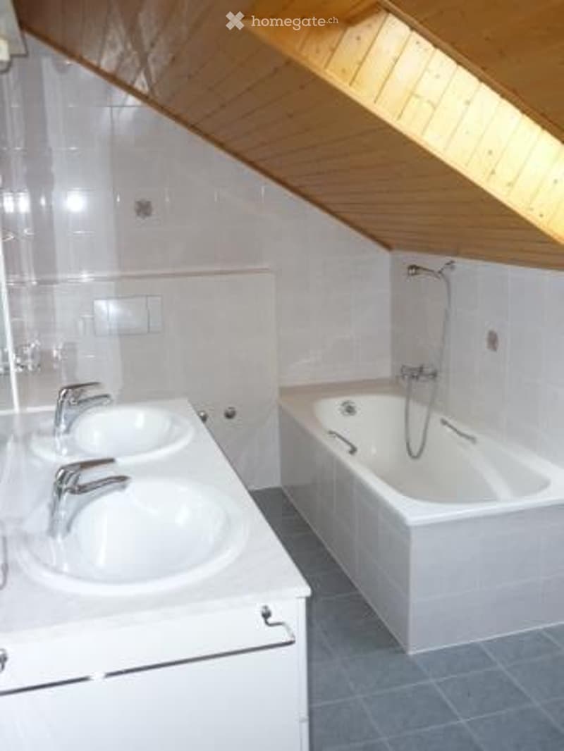 Modern bathroom with a double sink and a bathtub, featuring white tiles and a wooden slanted ceiling.