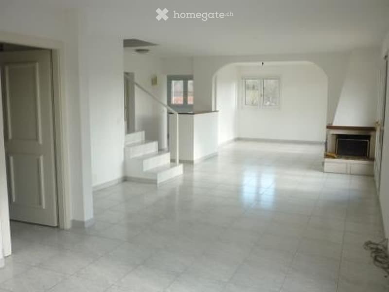 Empty living space with white walls, tiled floor, staircase leading to an upper level, fireplace, and large windows.
