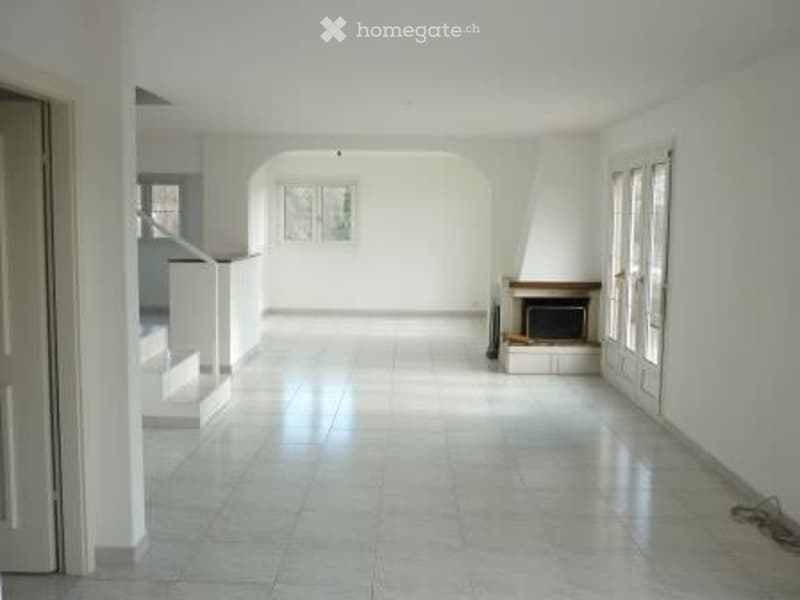 Empty room with white walls, tiled floor, fireplace, and large windows. No furniture or equipment present.