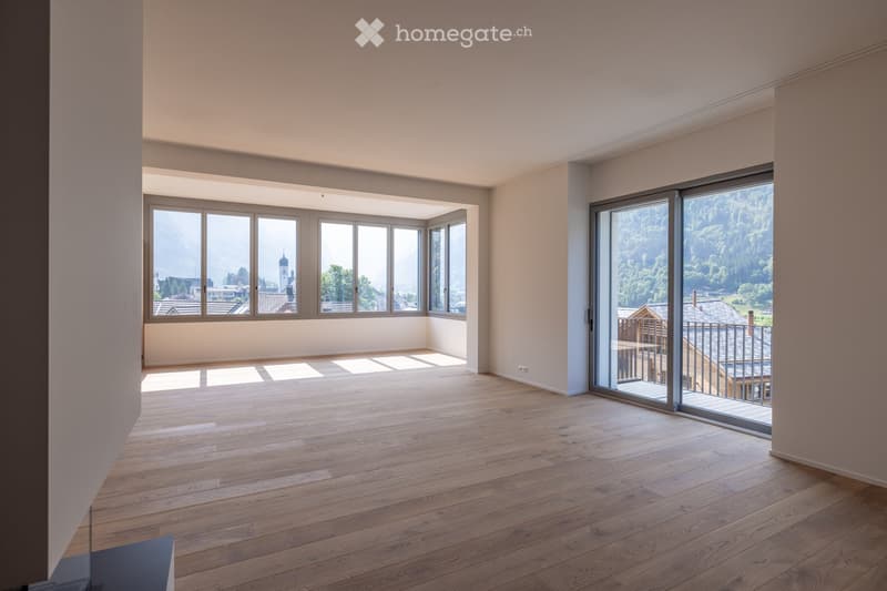 Empty room with wooden flooring, large windows, and a sliding glass door leading to a balcony with a scenic mountain view.