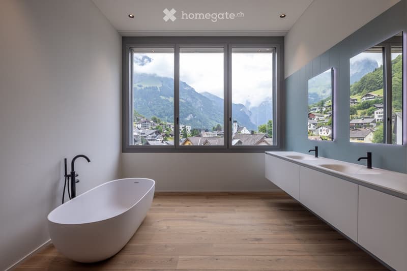 Modern bathroom with a freestanding bathtub, double sink vanity, large windows offering a scenic mountain view.