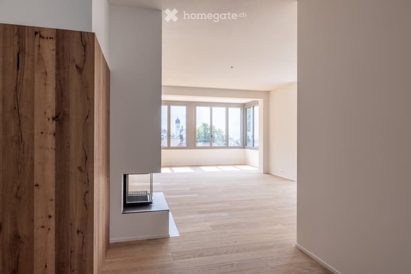 Empty room with wooden flooring, white walls, large windows, and a built-in fireplace.