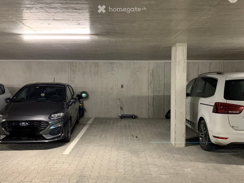 Underground parking area with two cars and a scooter parked, concrete walls and ceiling, tiled floor.