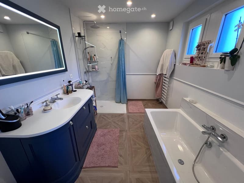 Modern bathroom with a double sink vanity, bathtub, large mirror, and shower area. Features wooden flooring, white walls, and decorative towels.