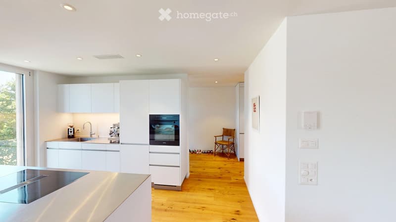 Modern kitchen with white cabinets, stainless steel appliances, wooden flooring, and a large window offering a view of greenery.