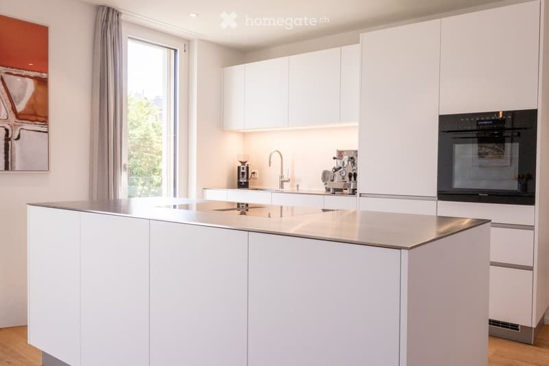Modern kitchen with white cabinets, a central island, stainless steel sink, coffee maker, and built-in oven.