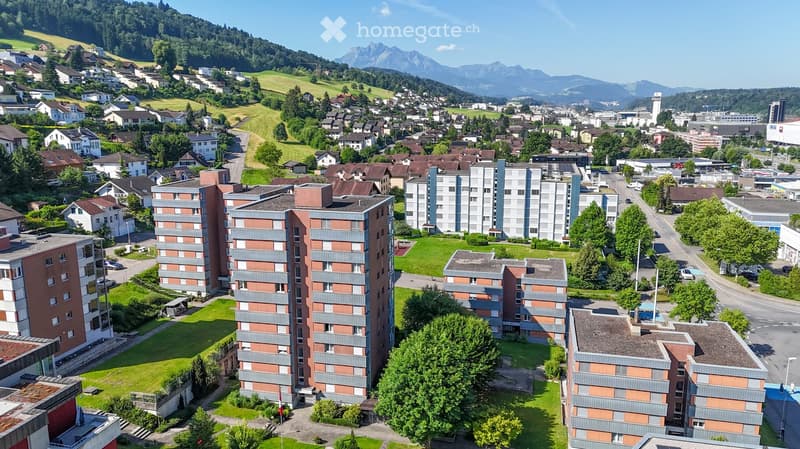 Aerial view of a residential area with multiple apartment buildings, green spaces, and surrounding mountains.