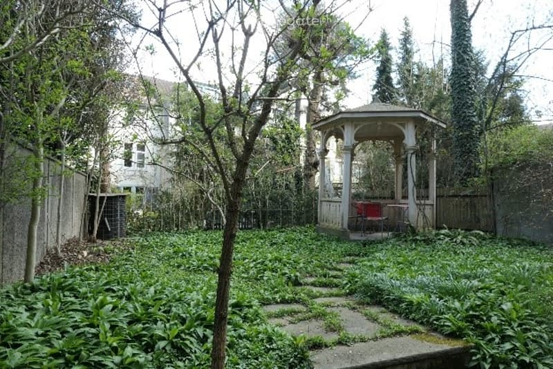 A lush garden with a gazebo, stone pathway, and surrounding greenery.