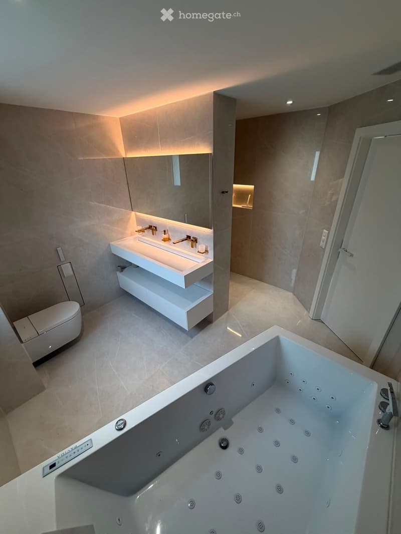 Modern bathroom with a large bathtub, double sink, and built-in storage, featuring sleek white fixtures and warm lighting.