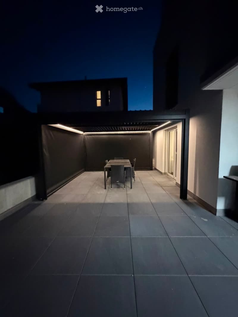 Modern outdoor dining area with a table and chairs, surrounded by sleek walls and illuminated by ambient lighting.