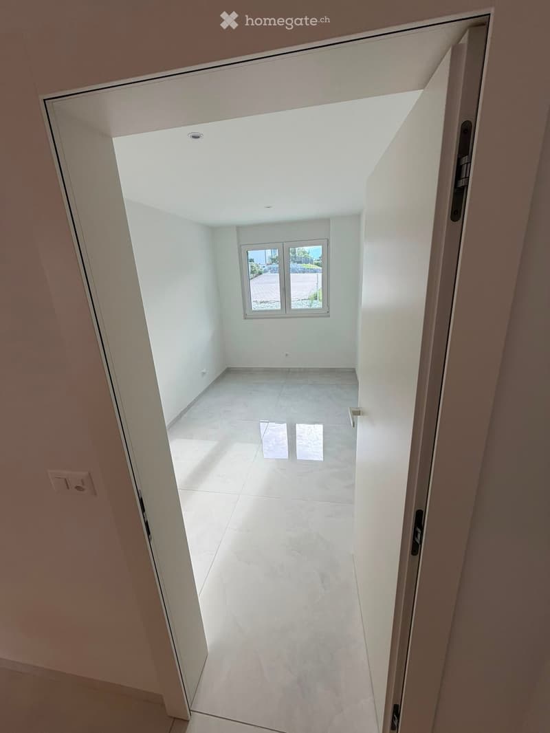 Empty hallway with white walls, tiled floor, and a window at the end providing natural light.