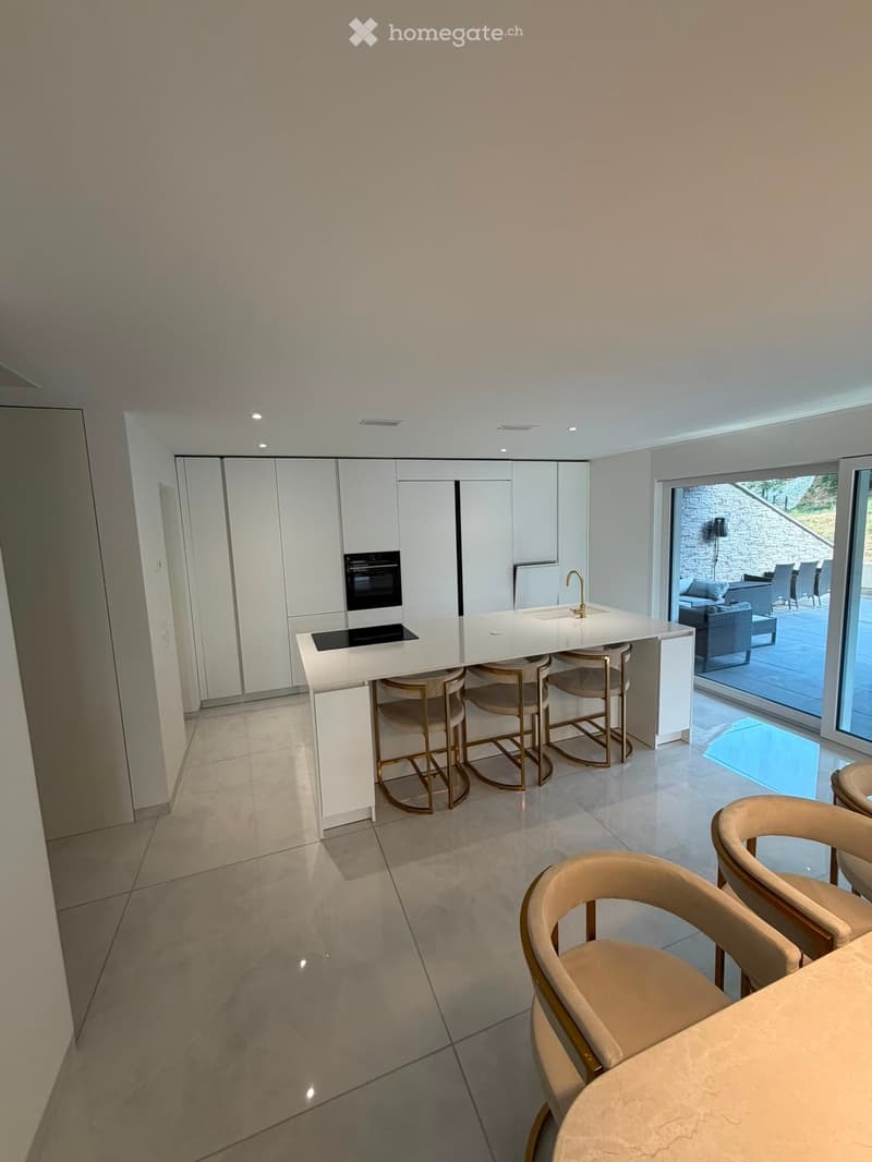 Modern kitchen with white cabinets, a central island with a built-in stove and sink, and beige chairs around a dining table.
