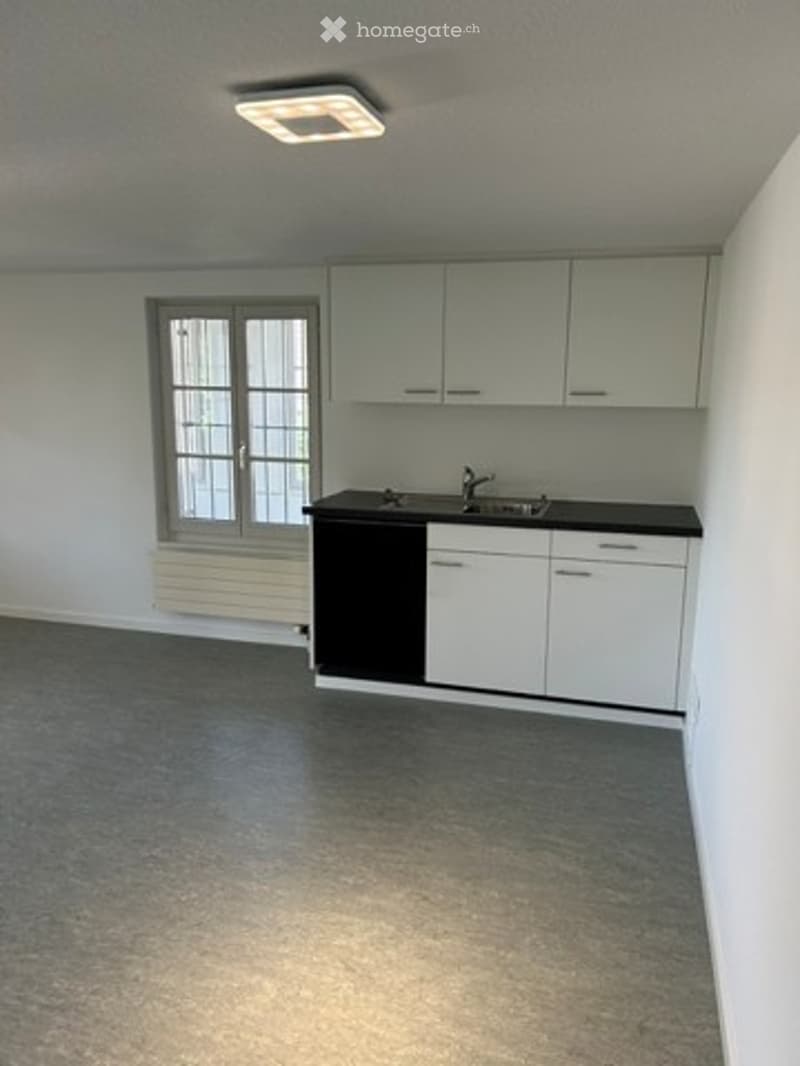 Empty kitchen with white cabinets, black countertop, sink, and a window with frosted glass panels. No furniture or appliances are present.